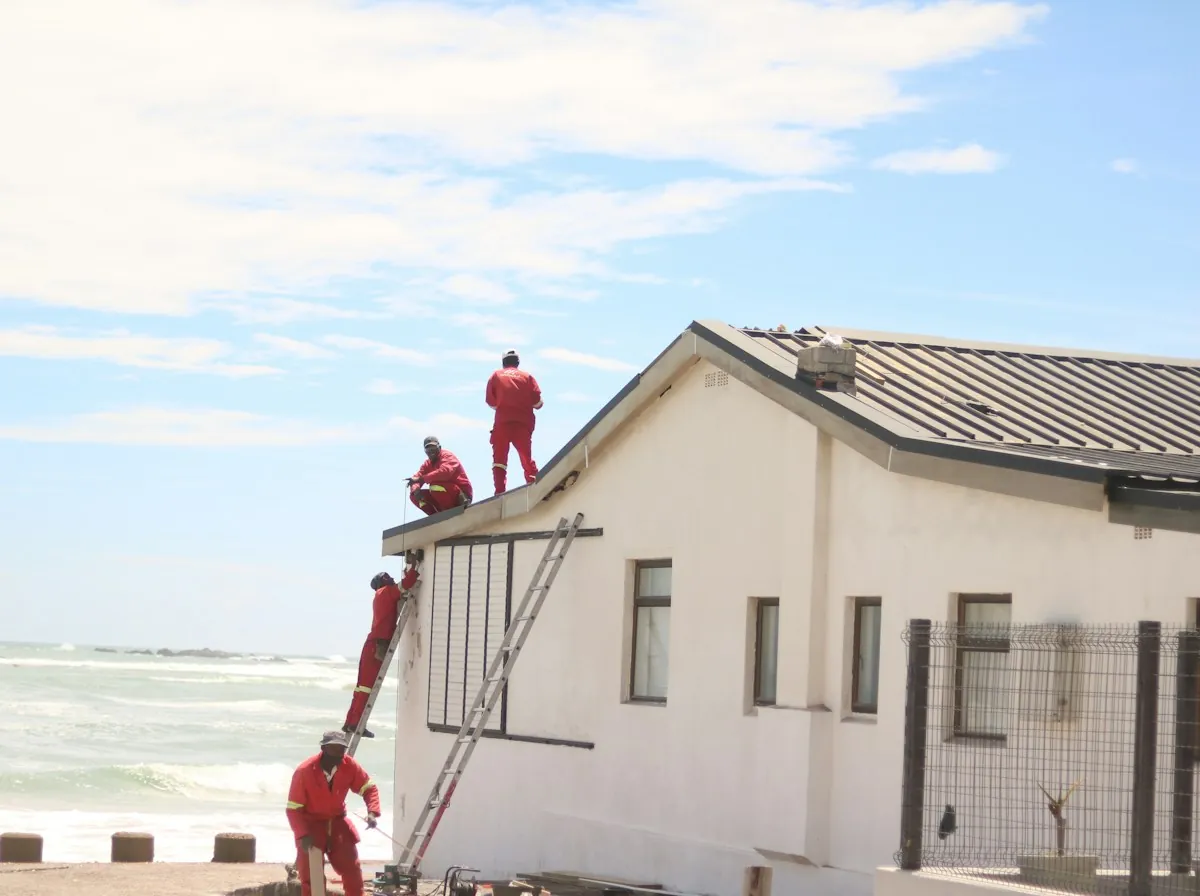 Roof Replacement in Hesperia — two roofers working on the roof of a white stucco house near the coast